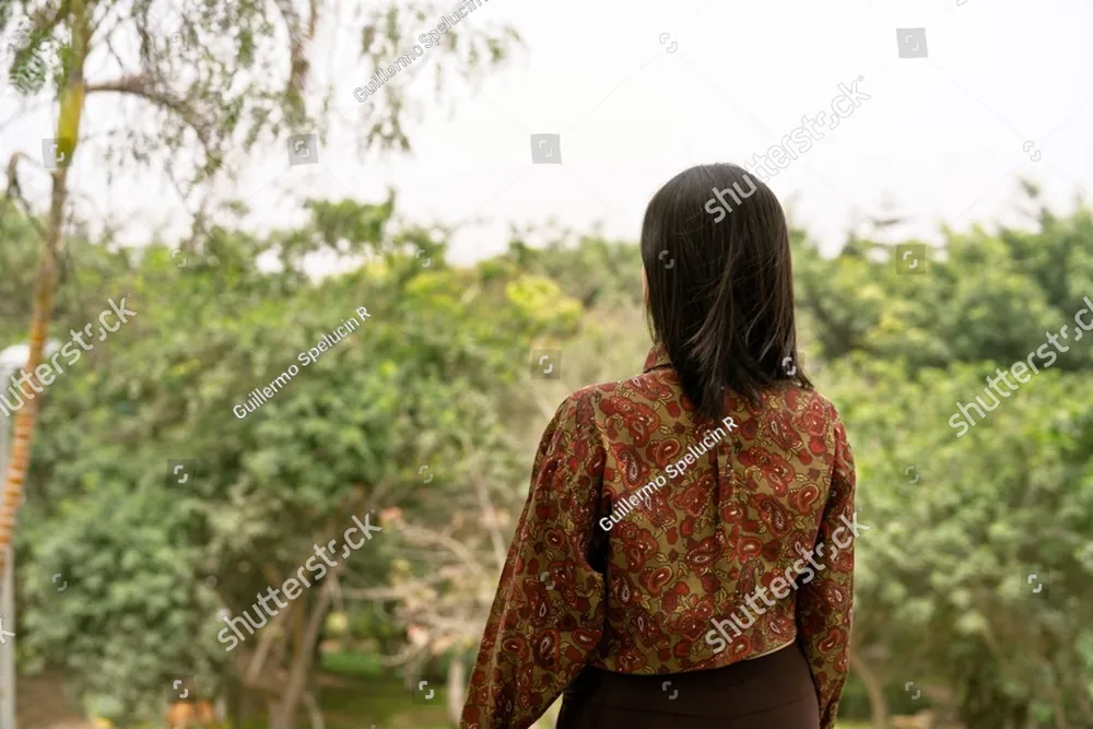 A woman with long dark hair walking into a green garden